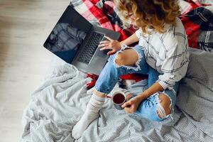 Stylish smart cheerful  woman in  eyeglasses using laptop , lying on cozy bed, drinking coffee. photo