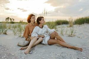 Summer fashion image of two  brunette european women in linen clothes posing on the beach photo