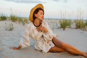 Beautiful european woman with short hairs demonstrate trendy summer look i on the beach. Linen clothes. Straw hat. photo