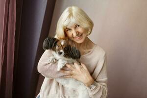 Portrait of happy  mature  woman lovingly hugging pet dog and smiling while enjoying weekend at home. Soft colors. photo