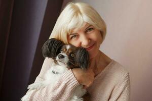 Portrait of happy  mature  woman lovingly hugging pet dog and smiling while enjoying weekend at home. Soft colors. photo