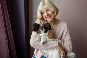 Portrait of happy  mature  woman lovingly hugging pet dog and smiling while enjoying weekend at home. Soft colors. photo