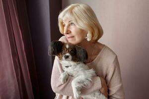 Portrait of happy  mature  woman lovingly hugging pet dog and smiling while enjoying weekend at home. Soft colors. photo