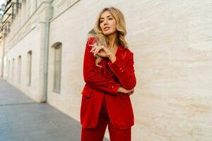 Profeshional fashion model in  elegant red velvet suit posin outdoor in old european city.    Blond wavy hairs, perfet skin, full lips. photo