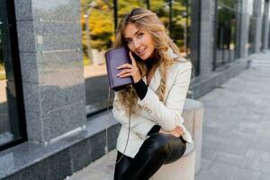 Sucsessful blond woman with perfect wavy hairs in casual  outfit with luxury purse posing over modern business center. photo