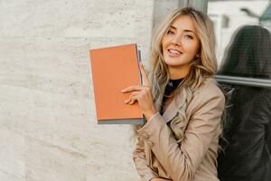 Close up photo of Elegant sucsessful blond  woman in stylish casual outfit posing   on the street. Holding advertising catalogs.