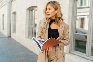 Sucsessful blond business woman posing in stylish suit outdoor. Holding  bdesigner catalogs. photo