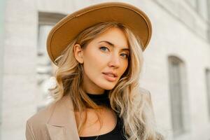 Fashion outdoor photo of stylish blond woman with perfect wavy hairs in beige hat and casual suit.