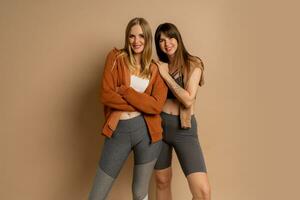 Two sportive women in stylish fitness cwear posing  on beige background. Healthy lifestyle concept. photo