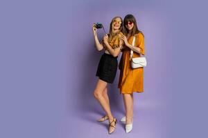 Two pretty women , best friends, posing on purple background in trendy  summer outfit. Full lenght. photo