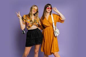 dos bonito mujer , mejor amigos, posando en púrpura antecedentes en de moda verano atuendo. foto