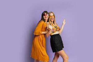 dos juguetón elegante mujer posando en estudio terminado púrpura antecedentes. amigos bailando y teniendo divertida. foto