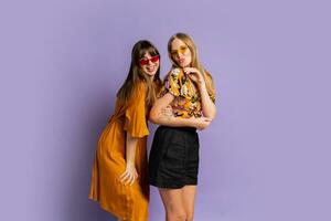 Two playful stylish women posing in studio over purple background. Friends dancing and having fun. photo