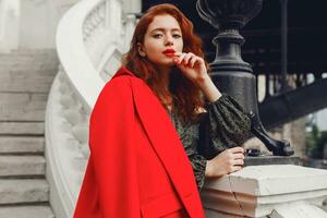 Lovely ginger female with perfect white skin looking forward. Wearing stylish red jacket and green silk dress. Wavy hairstyle. Paris fashion look. photo