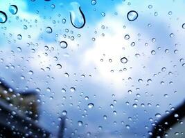 Blurred water droplet or raining on glass with building, electrical pole, blue sky and cloud background concept photo