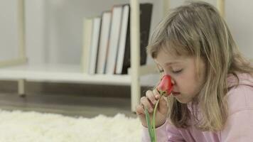 un' poco ragazza è seduta su il pavimento con un' fiore nel sua mano video