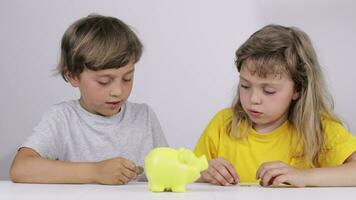 two children sitting at a table with a piggy bank video