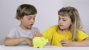 two children sitting at a table with a piggy bank video