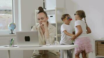 een vrouw zittend Bij een bureau met een laptop met kinderen spelen in de omgeving van video