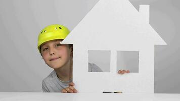 een jongen vervelend een moeilijk hoed Holding een papier huis video