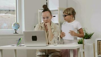 een vrouw zittend Bij een bureau met een laptop met kinderen spelen in de omgeving van video