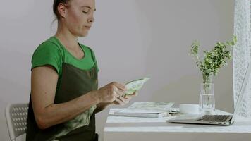 a woman sitting at a table with a laptop and a green apron video