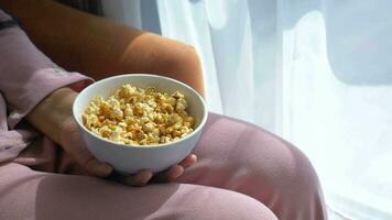 young women eating popcorn sitting on sofa at home . video