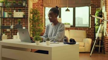 Zuhause basierend afrikanisch amerikanisch unabhängig Arbeiter beginnt Tag durch Abschluss Hausarbeit zum online Arbeit. weiblich Telearbeiter und Individuell Blogger mit Laptop beim Arbeitsplatz zu Antworten zu E-Mails. video