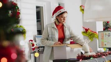 Vindictive worker packs desk belongings and steals Christmas office ornament on last day at work. Resentful woman getting fired from job during year end layoffs, taking revenge in frustration video