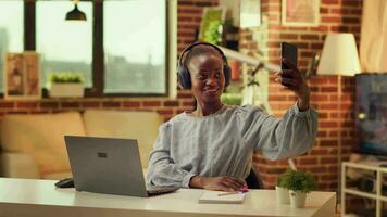 africano americano mulher levando selfies às lar, usando dourado hora pôr do sol luz para ter ótimo As fotos em Smartphone. trabalhador autonomo multitarefa com fotos e diariamente conectados tarefas. video