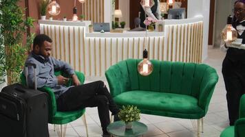 gäst läser texter på telefon på reception, väntar för registrering former till do kolla upp i bearbeta och ser rum. manlig turist använder sig av webb browser på smartphone väntar till Registrera på fem stjärna hotell. video