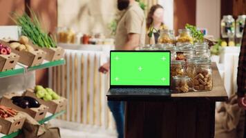 Chroma key laptop with copy space used as commercial sign in sustainable local shop. Promotional ad on green screen device in food store with products in reusable glass jar package video