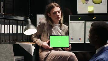 Kaukasisch privaat detective houdt tablet met groene scherm, net zo zwart politieagent onderzoekt een geïsoleerd copyspace Scherm. in kantoor, twee detectives gebruiken digitaal apparaat met Chroma sleutel mockup sjabloon. video