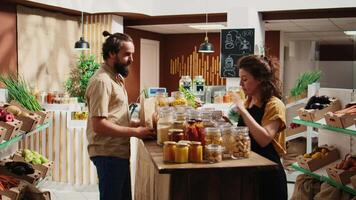 Man in zero waste supermarket using paper bag while shopping for vegetables, receiving info from storekeeper. Client in local shop with no single use plastics policy receiving help from vendor video