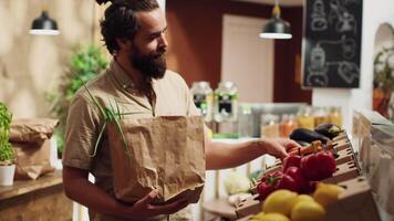 vegano homem dentro zero desperdício supermercado usando biodegradável papel saco enquanto compras para bio legumes. cliente dentro carbono neutro local mercearia fazer compras com não solteiro usar plásticos política video