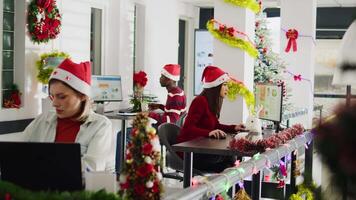 trabajo duro multicultural empleados trabajando durante Navidad temporada en festivo decorado oficina. diligente bipoc compañeros de trabajo ingresando datos en ordenadores en diverso Navidad florido lugar de trabajo video