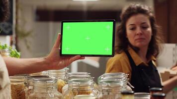 Man uses landscape mockup tablet in sustainable zero waste supermarket to check ingredients for healthy recipe. Vegan client in sustainable local shop with chroma key device shops for pantry staples video