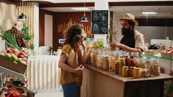 Client talking with seller in sustainable bio shop, inquiring about food items ethical sourcing and asking for recommendations. Woman in local store chatting with trader about pantry staples video