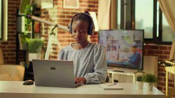 pigiste écoute à la musique et résolution du quotidien projet Tâches, chanceux à être soi employé. africain américain femme en chantant Chansons tandis que elle travaux sur responsabilités de le confort de sa chaud maison. video