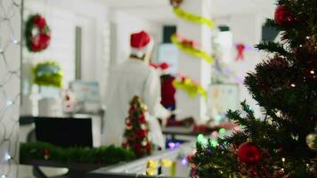 zoom in schot Aan medewerkers brainstorming ideeën voor project gedurende Kerstmis seizoen in feestelijk versierd kantoor. arbeiders in multicultureel werkplaats sieren met Kerstmis lichten en slingers video