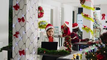 Happy multiethnic team working on christmas season in decorated office. Cheerful employees solving tasks at desk in diverse workplace next to colleagues during winter festive time video