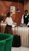 Vertical Video Senior couple paying for room reservation with credit card at front desk, using pos transaction after finishing check in process. Older man making electronic payment at all inclusive