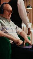 Vertical Video Retired person watches film on laptop using online streaming services, passing time while he is waiting to see accommodation. Old traveller enjoys movie on personal computer in lobby.