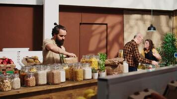 Zoom in shot of man in zero waste supermarket using nonpolluting paper bag while shopping for pantry staples. Client in local shop using no single use plastics policy to reduce greenhouse gas video