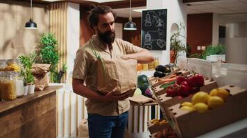 dolly in dichtbij omhoog schot van Mens in nul verspilling supermarkt gebruik makend van niet-vervuilend papier zak terwijl boodschappen doen voor groenten. cliënt in lokaal winkel gebruik makend van Nee single gebruik kunststoffen het beleid voor co2 uitstoot vermindering video