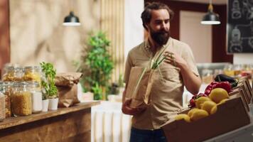 Man in zero waste store using paper bag, shopping for vegetables, feeling dopamine rush while smelling them. Client experiencing bliss trying product in local shop with no single use plastics policy video