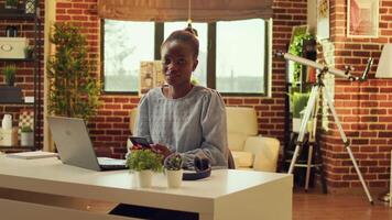 Woman freelancer navigating webpage and checking social media app before solving daily tasks, network connection. African american self employed teleworker sitting at desk at sunset. video