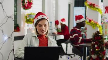 Dolly out portrait shot of happy employee working on christmas season in decorated office. Cheerful worker solving tasks at desk in diverse xmas ornate workplace next to colleagues video