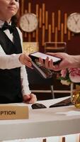 Vertikale Video Alten Mann macht nfc Transaktion mit Handy, Mobiltelefon Telefon beim pos Terminal, bezahlen zum Unterkunft beim fünf Star Erholungsort. Tourist ankommen beim Vorderseite Schreibtisch tun prüfen im zum Urlaub. schließen oben