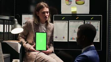 Female investigator grasps device with greenscreen to present mockup display, conducting criminal investigation. Male detective speaks with policewoman holding tablet with isolated copyspace template. video